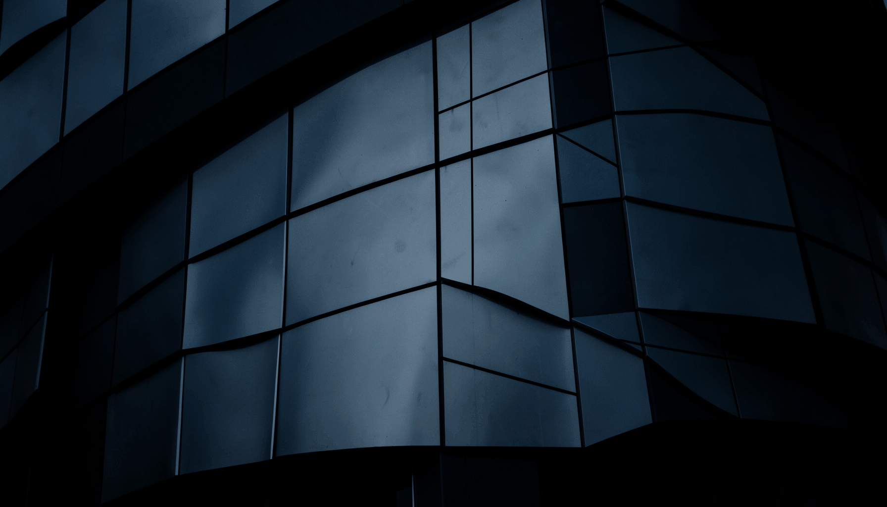 Low-key architectural detail shot of shaped aluminum panels on a curved building exterior, rich blue-gray tones with dramatic shadow
