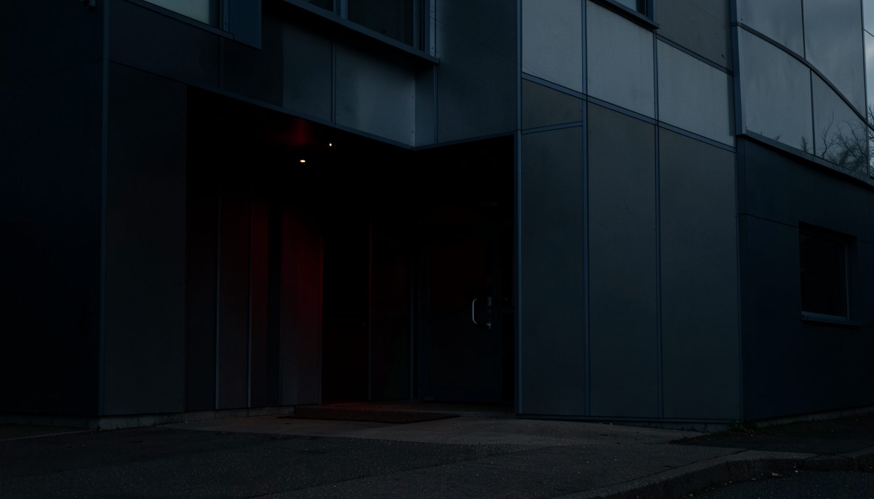 Moody photograph of an institutional building entrance with aluminum panel cladding, navy and charcoal tones under overcast light
