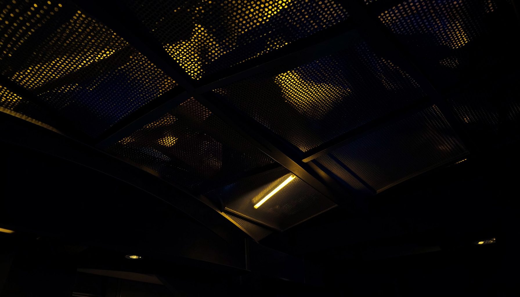 Dark architectural interior with curved perforated metal ceiling panels and warm ambient lighting, deep navy and gold tones