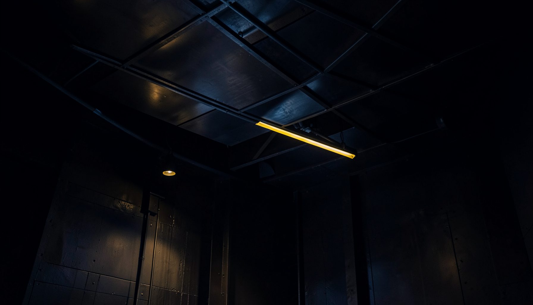 Dark industrial interior with suspended aluminum ceiling panels and warm accent lighting, deep navy and charcoal tones
