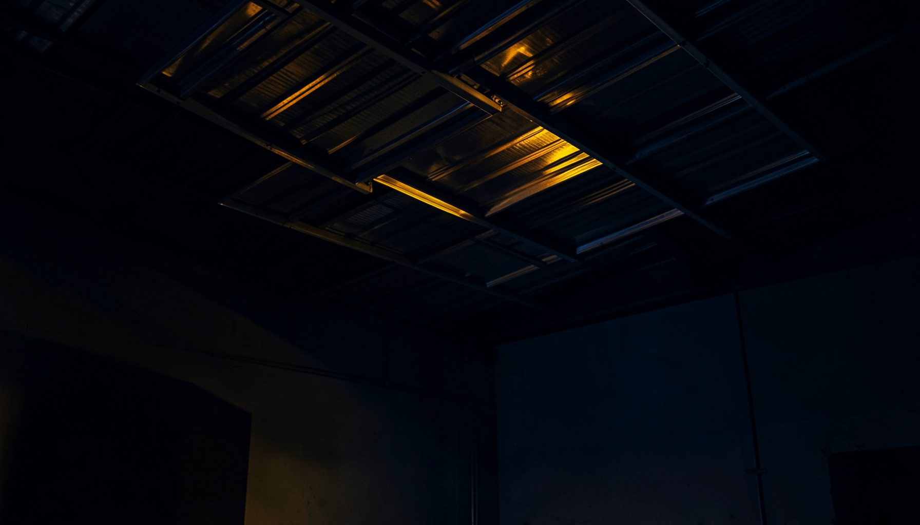 Dark industrial interior with suspended aluminum panel ceiling systems, warm amber accent lighting against deep navy shadows