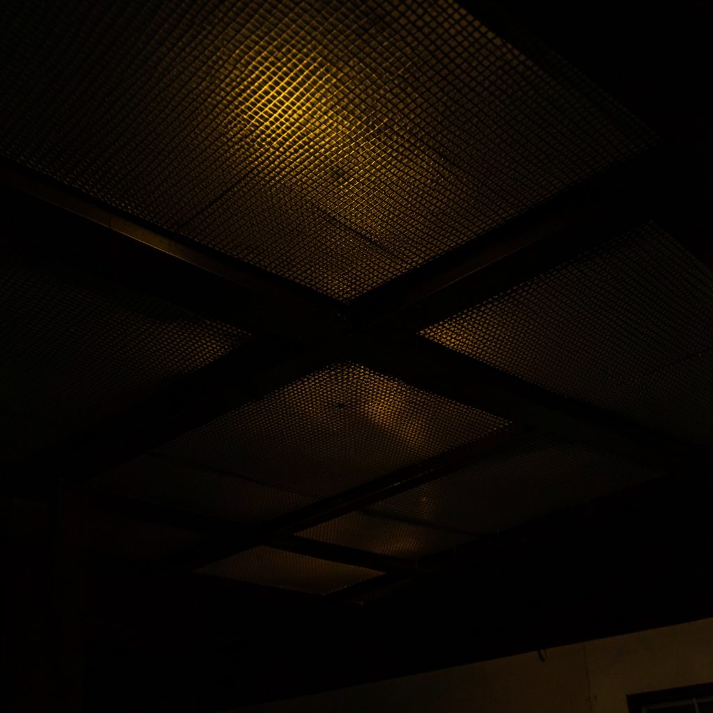 Dark interior ceiling with continuous expanded mesh aluminum panels, warm ambient lighting