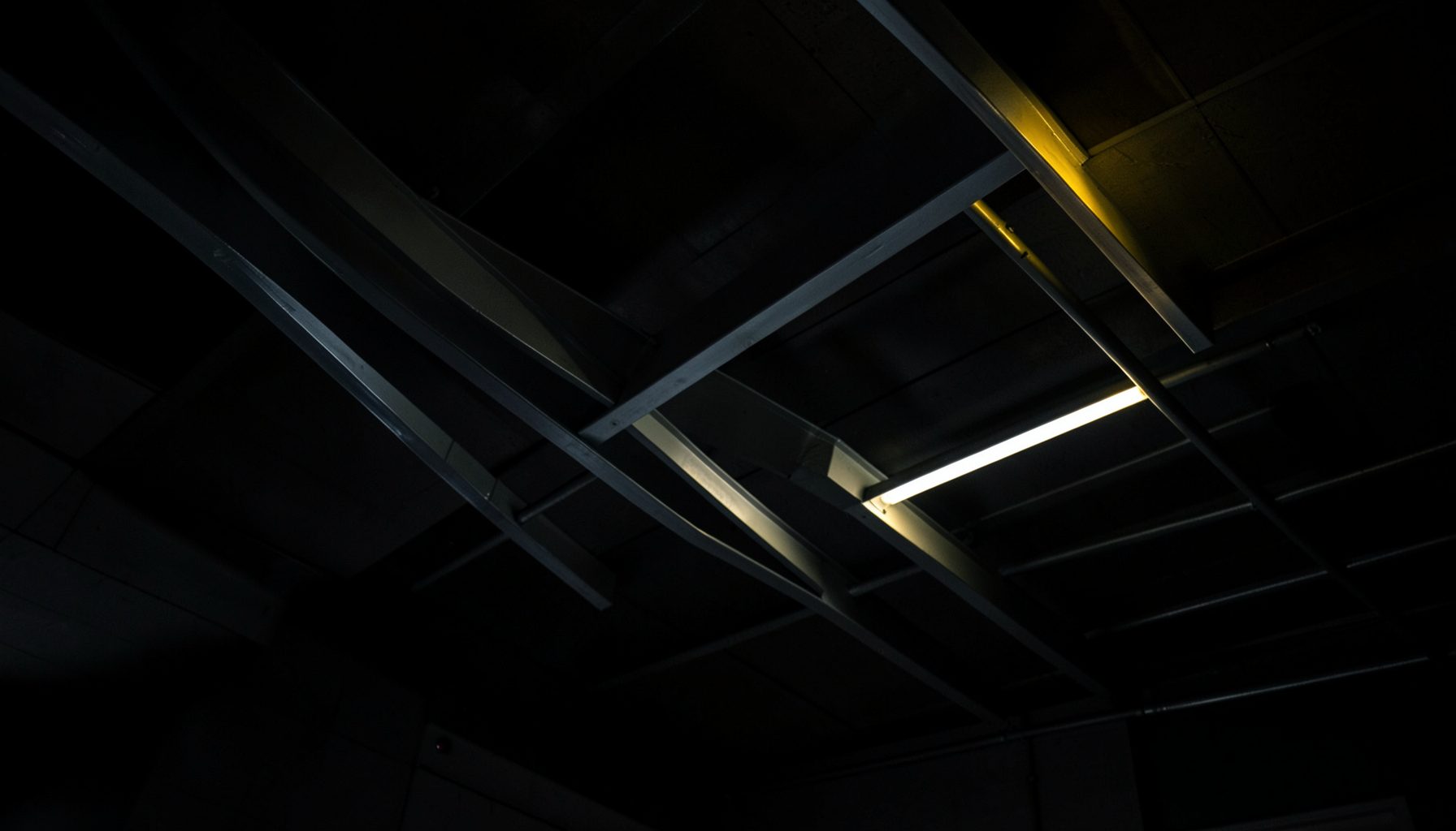 Curved aluminum square tubes sweeping in a dramatic arc across a ceiling, dark metallic gray finish with subtle reflections
