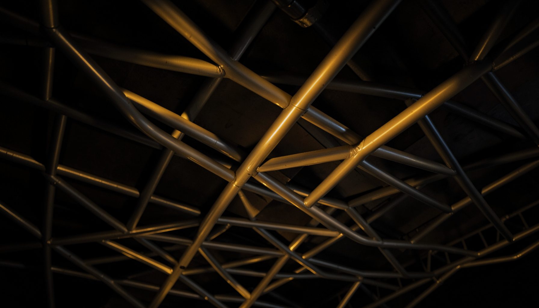 Architectural ceiling with intersecting shaped aluminum tubes forming a geometric grid, warm gray metallic finish